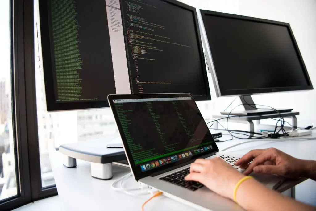 A developer working on code across a laptop and multiple monitors
